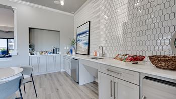 A kitchen with white cabinets and a white tiled wall.